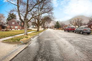 View of asphalt street with a residential view, sidewalks, a mountain view, and curbs