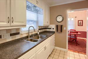 Kitchen featuring dark countertops, white cabinets, white dishwasher, crown molding, and decorative backsplash