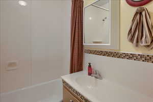Bathroom featuring vanity, shower / tub combo, and backsplash
