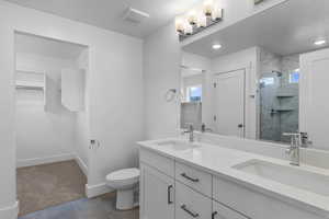 Full bath featuring double vanity, a shower stall, dark tile patterned flooring, recessed lighting, and a walk in closet