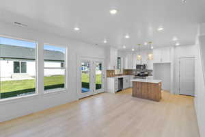 Kitchen featuring a kitchen island, dual tone cabinetry, stainless steel appliances, light wood finished floors, and backsplash