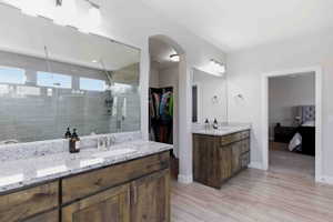 Ensuite bathroom with a spacious closet, two vanities, light wood finished floors, and a stall shower