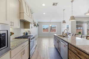 Dual tone kitchen with stainless steel appliances, light stone counters, hanging light fixtures, wood finish floors, and tasteful backsplash
