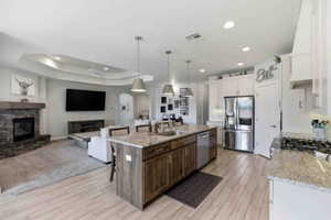 Kitchen with open floor plan, a breakfast bar, stainless steel appliances, light stone countertops, and a stone fireplace