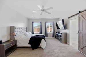 Bedroom featuring a barn door, light carpet, and a ceiling fan