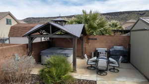 Fenced backyard with area for grilling, a patio area, a gazebo, a hot tub, and a mountain view