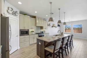 Two tone kitchen featuring light stone counters, stainless steel appliances, a breakfast bar area, wood tiled floors, and decorative light fixtures