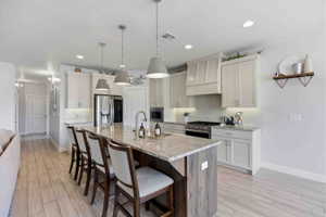 Dual tone kitchen featuring a breakfast bar area, stainless steel appliances, wood finish floors, decorative backsplash, and a center island with sink