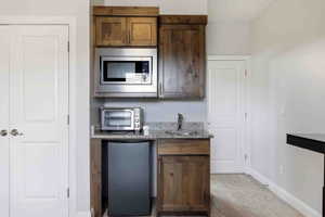 Kitchen featuring light stone countertops, stainless steel appliances, dark wood finish cabinetry, and light colored carpet