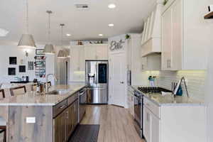 Two tone kitchen featuring a kitchen breakfast bar, stainless steel appliances, light stone countertops, an island with sink, and decorative backsplash