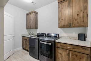 Laundry area with washing machine and clothes dryer, light wood-style floors, and cabinet space