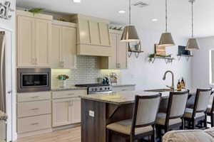 Two tone kitchen with a kitchen island with sink, light stone countertops, a kitchen bar, decorative light fixtures, and backsplash