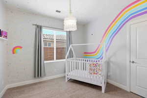 Bedroom featuring light colored carpet, a nursery area, and wallpapered walls