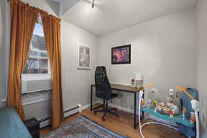 Office featuring light wood-style floors, a baseboard radiator, a textured wall, and cooling unit