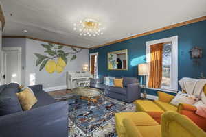 Living room featuring hanging lights, wood finished floors, a baseboard heating unit, and crown molding