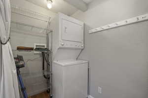 Laundry room with a textured wall and stacked washer and clothes dryer