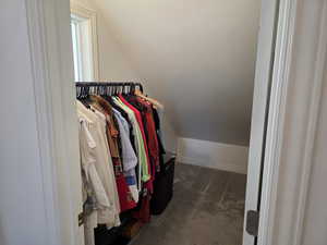 Master walk in closet with vaulted ceiling and dark colored carpet