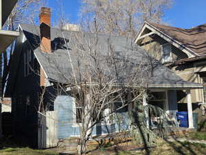 View of side of property featuring a chimney, a porch, and roof with shingles