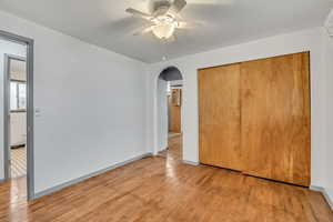Unfurnished bedroom featuring light wood-style flooring, arched walkways, a closet, and ceiling fan