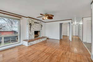 Unfurnished living room with ceiling fan, arched walkways, light wood-style floors, a stone fireplace, and ornamental molding
