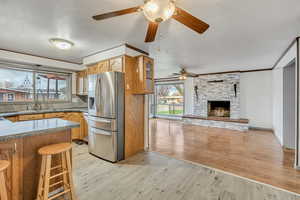 Kitchen with stainless steel fridge with ice dispenser, light wood-style floors, glass fronted cabinets, a fireplace, and ornamental molding