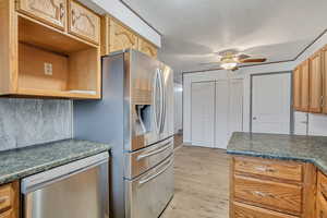 Kitchen with dark countertops, stainless steel appliances, light wood finished floors, and a ceiling fan