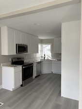Kitchen with stainless steel appliances, white cabinets, and light wood finished floors
