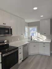 Kitchen featuring stainless steel appliances, white cabinetry, recessed lighting, light wood-type flooring, and light stone countertops