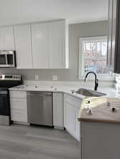 Kitchen featuring stainless steel appliances, white cabinetry, light wood-style flooring, and light stone counters