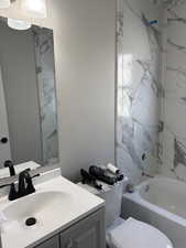 Full bathroom featuring vanity, a textured wall, and a combined bath / shower with marble appearance