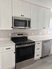 Kitchen with stainless steel appliances, light stone countertops, and white cabinetry