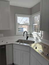 Kitchen featuring dishwashing machine, white cabinets, and light stone counters