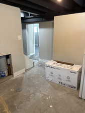 Unfinished basement with baseboards and white refrigerator