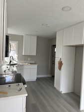 Kitchen with white cabinetry, light wood finished floors, light countertops, black microwave, and electric range