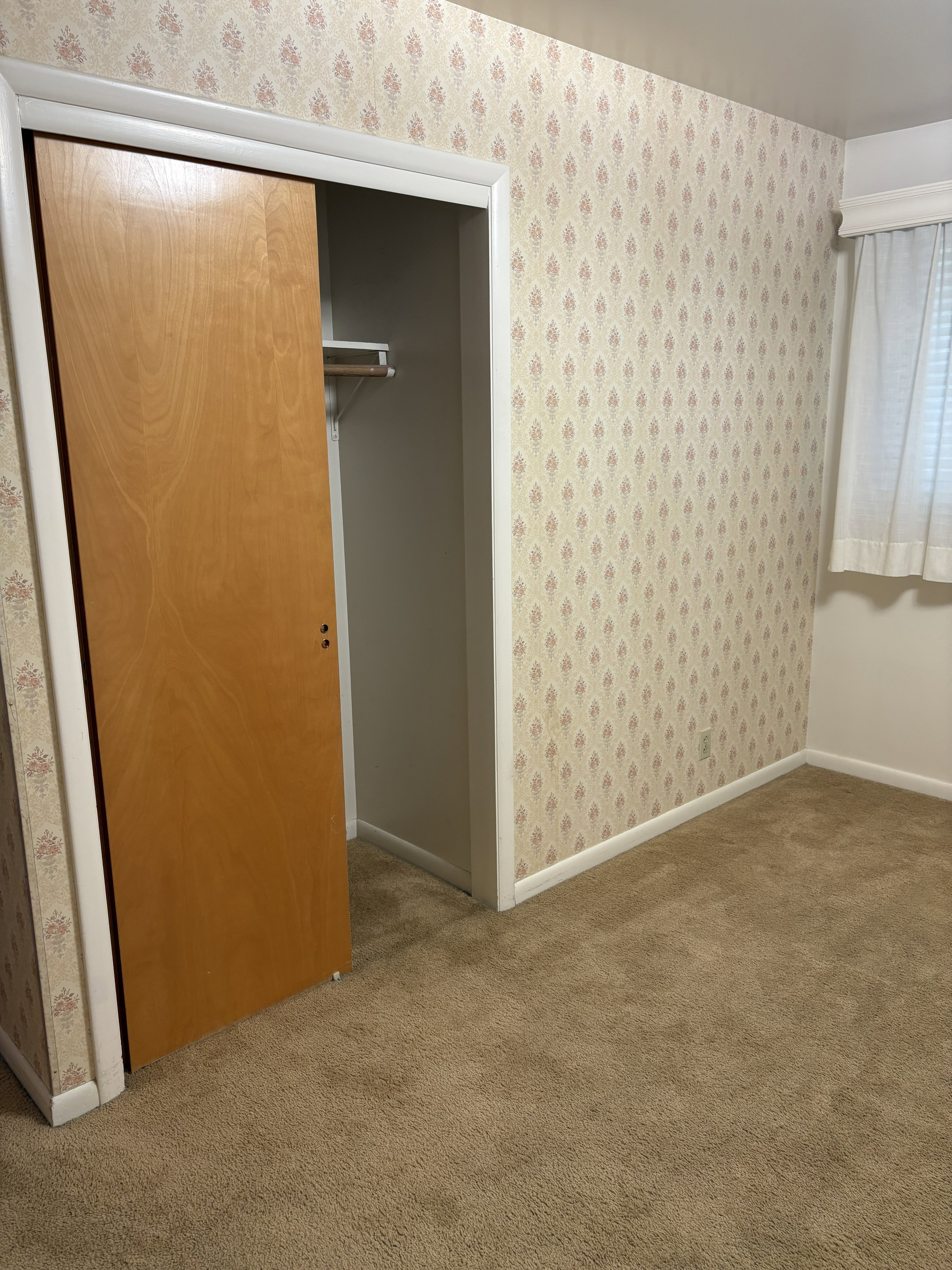 Bedroom featuring patterned wallpaper, neutral carpet flooring, and a closet with a natural wood-finish sliding door