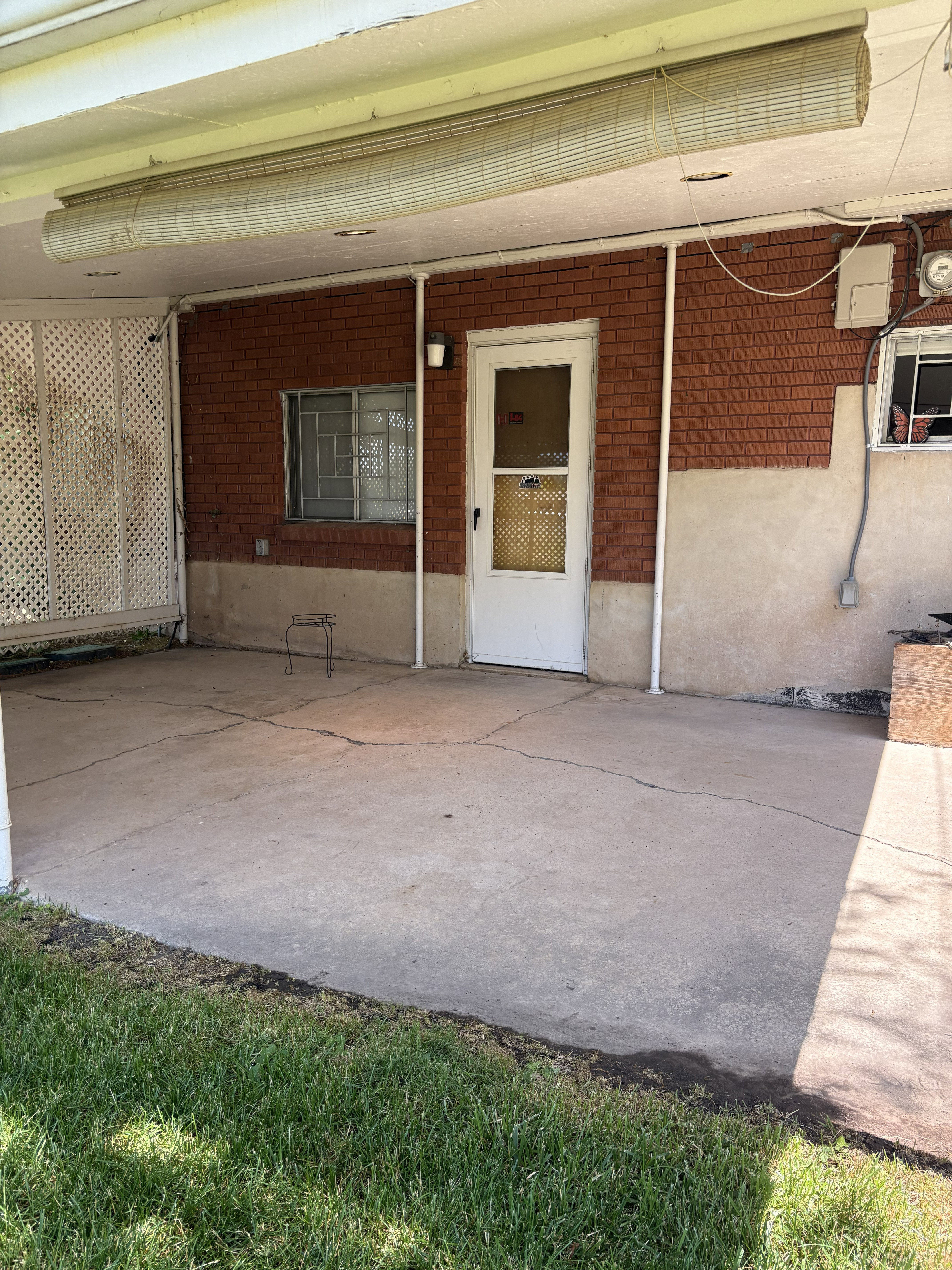 Covered patio with a concrete surface, brick exterior wall, white entry door, and security window bars