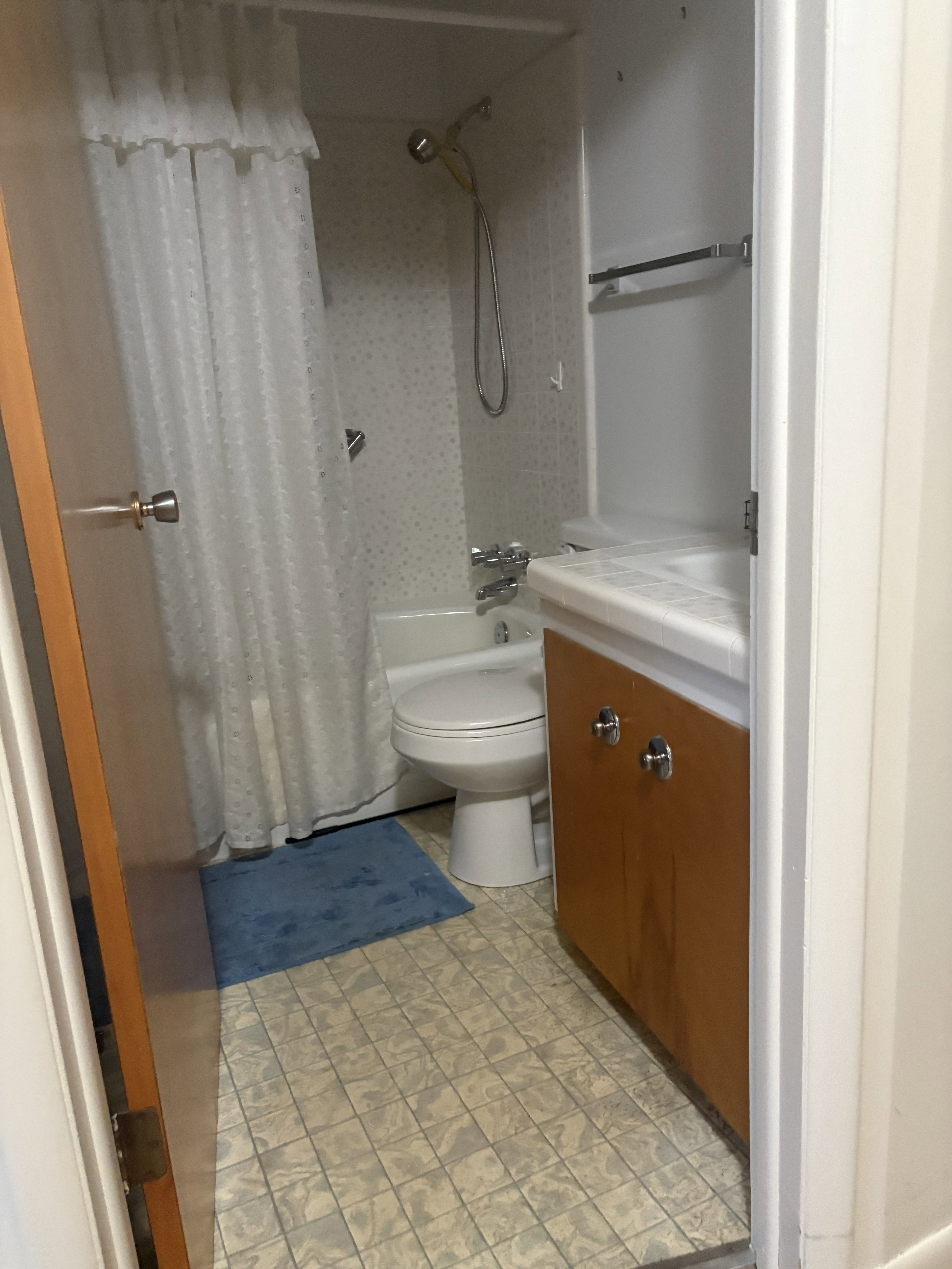 Compact bathroom featuring a shower-over-tub combination, a toilet, a vanity with wood-finish cabinetry, and patterned floor tiles