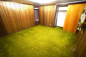 Unfurnished bedroom featuring carpet, wooden walls, and a closet