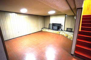 Finished basement with wooden walls, brick patterned flooring, and a wood stove