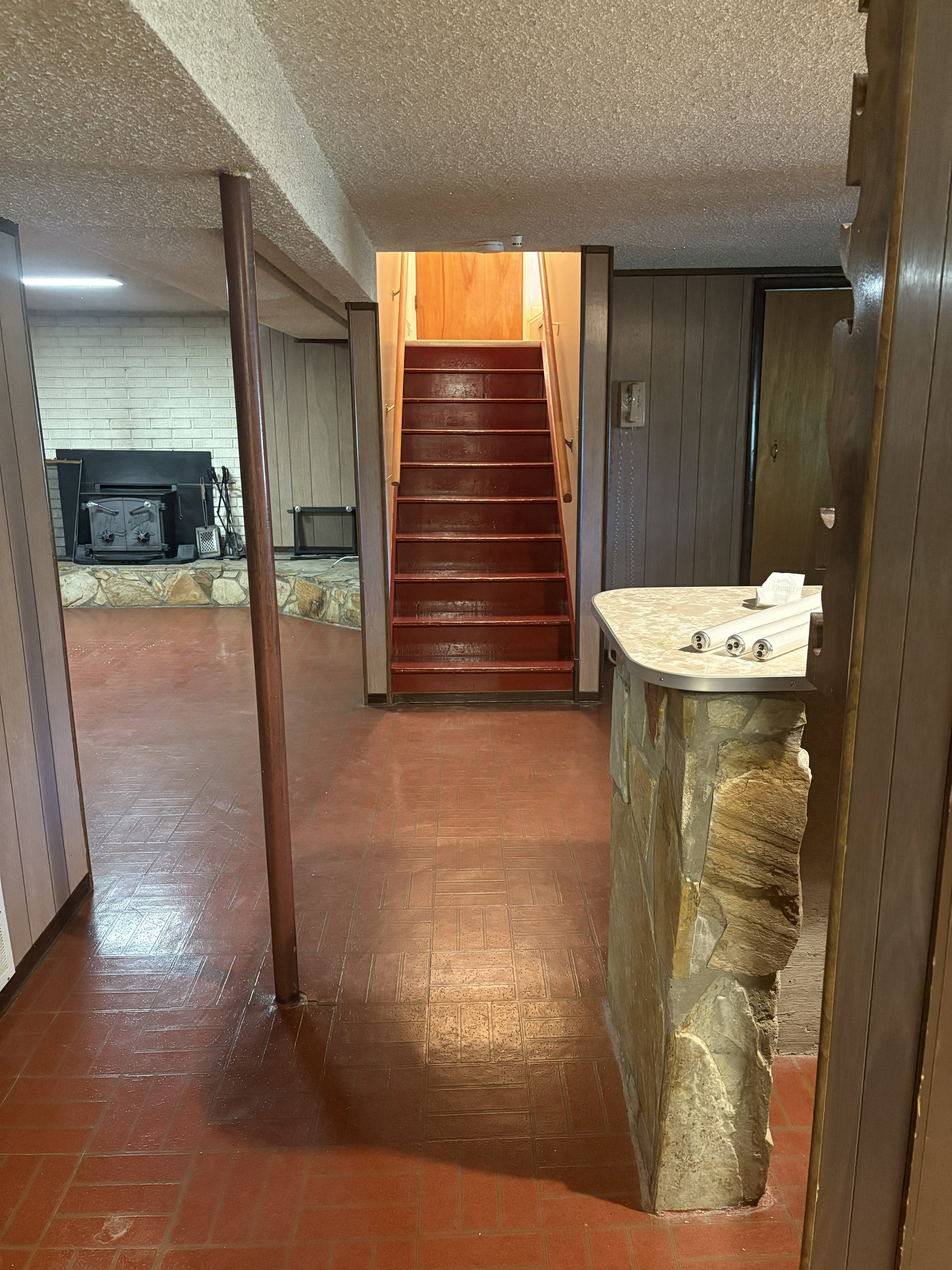 Finished lower level featuring a stone-clad wet bar, wood-finish stairs, tile flooring, and a white brick fireplace with a stone hearth