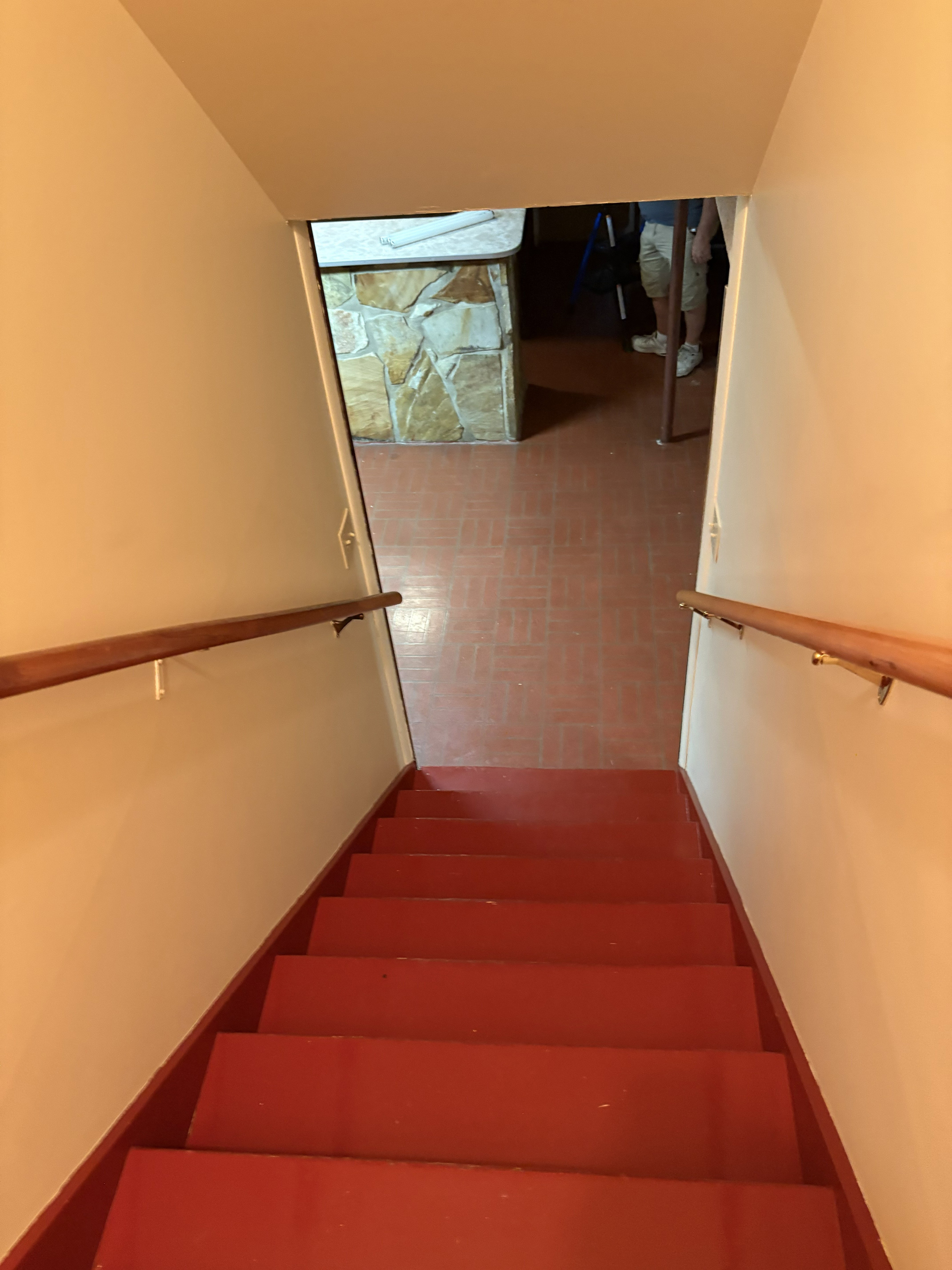 Staircase with red-painted treads and risers, featuring a light wood handrail on both sides