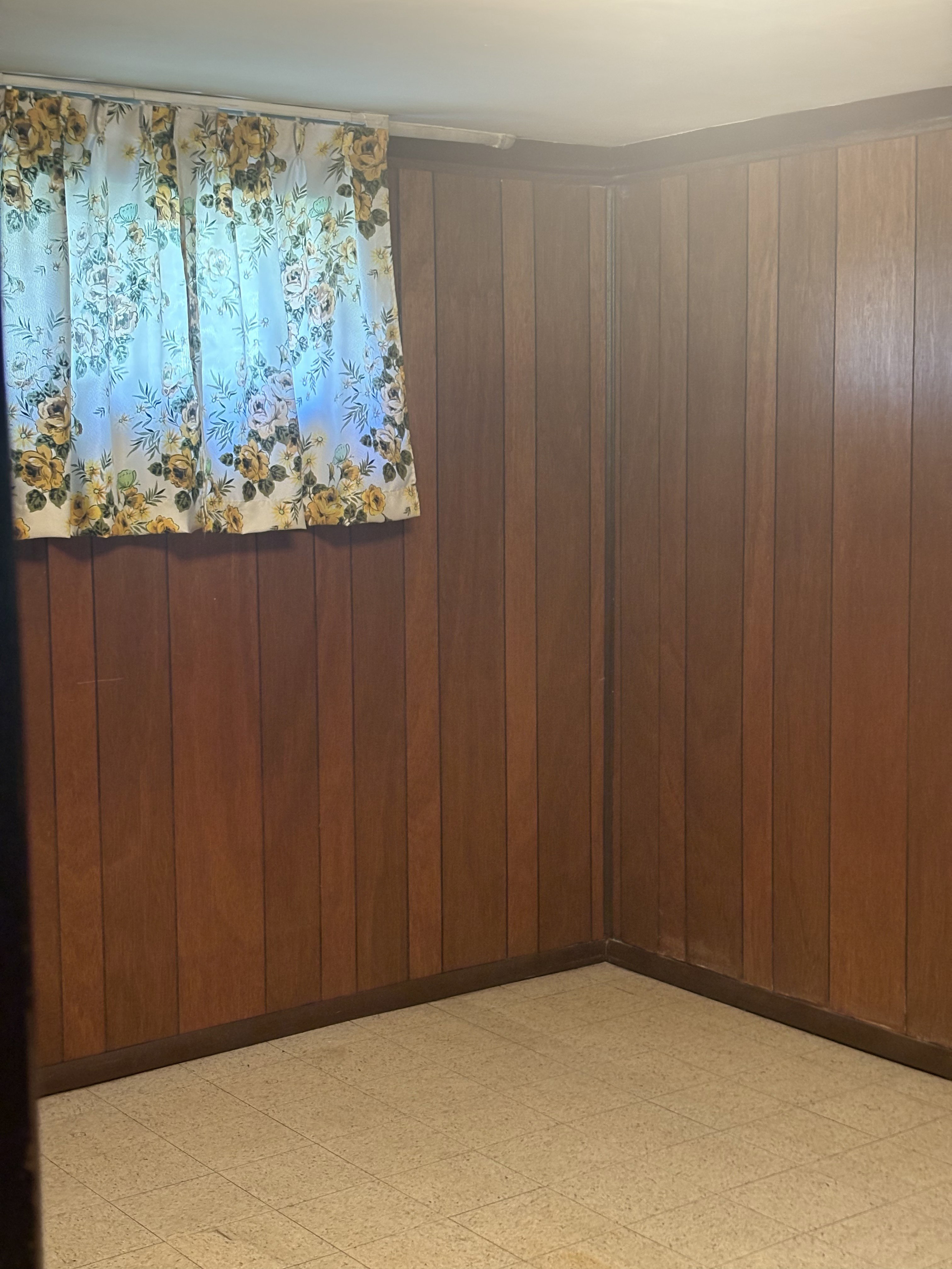 Room featuring wood paneling on walls, light-toned tiled flooring, and a single window