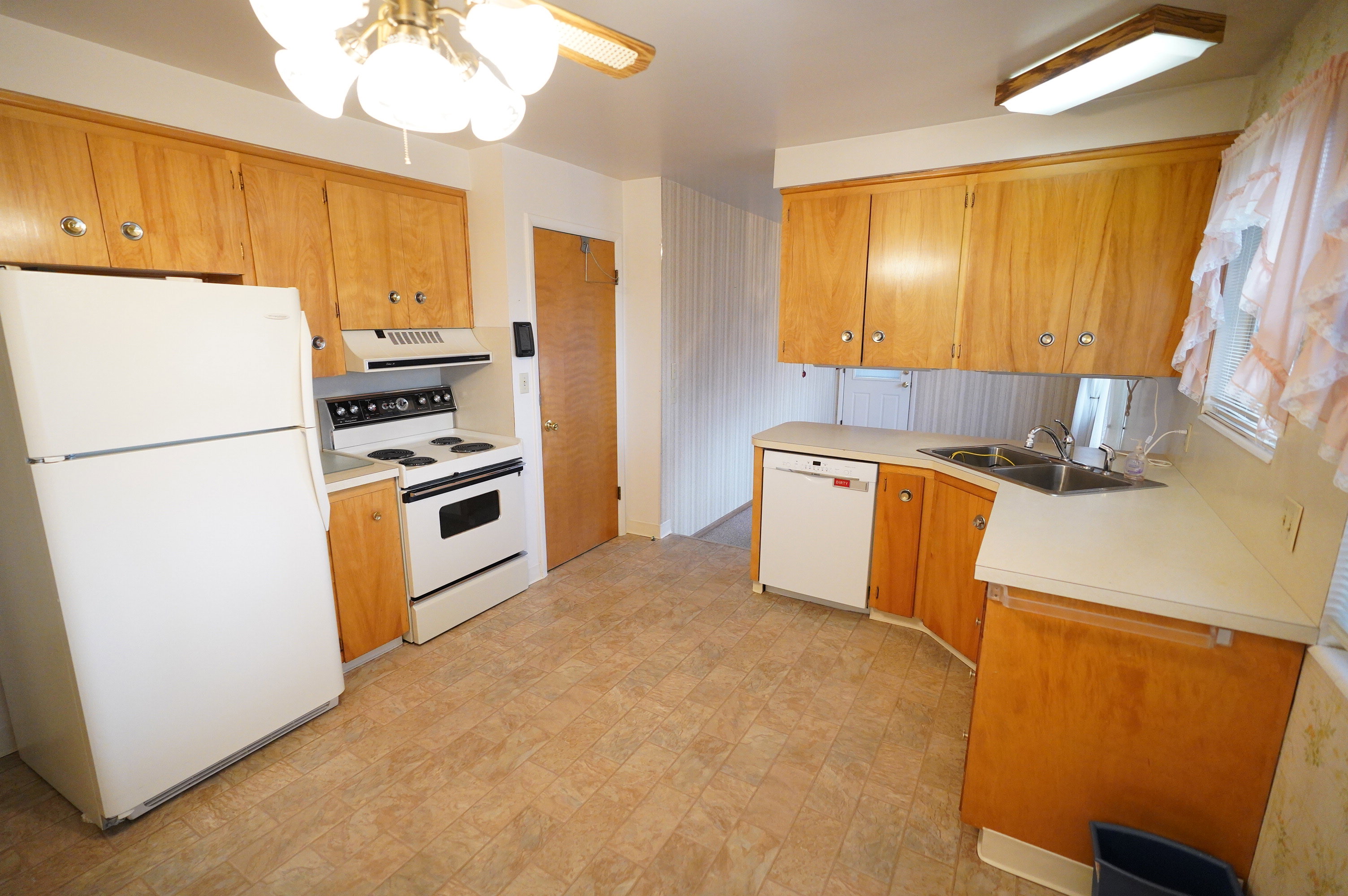 Kitchen featuring white appliances, a peninsula, light countertops, a ceiling fan, and wood finish cabinets