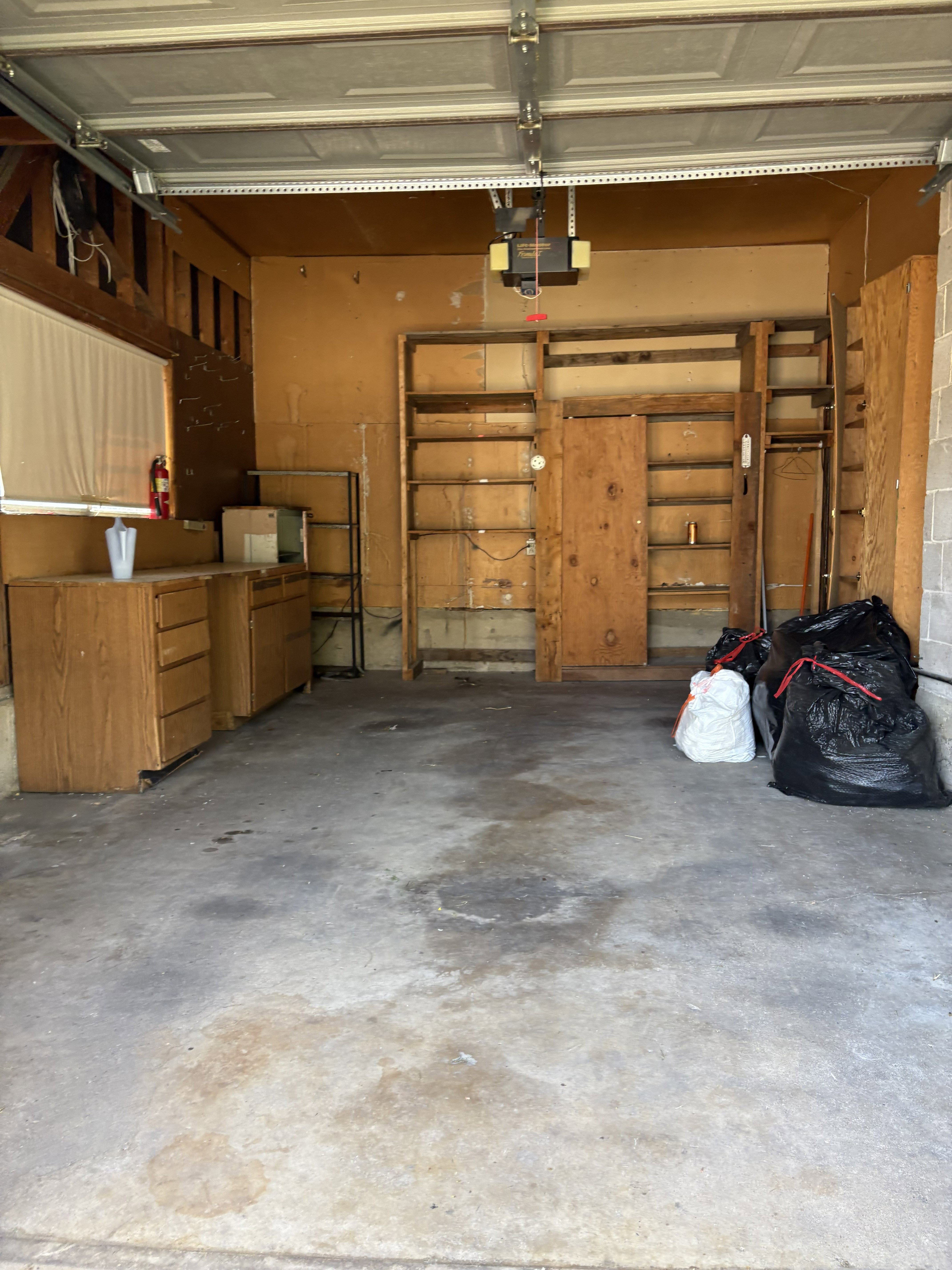 Attached garage featuring a concrete floor, overhead garage door with opener, built-in shelving, and wood-finish cabinetry