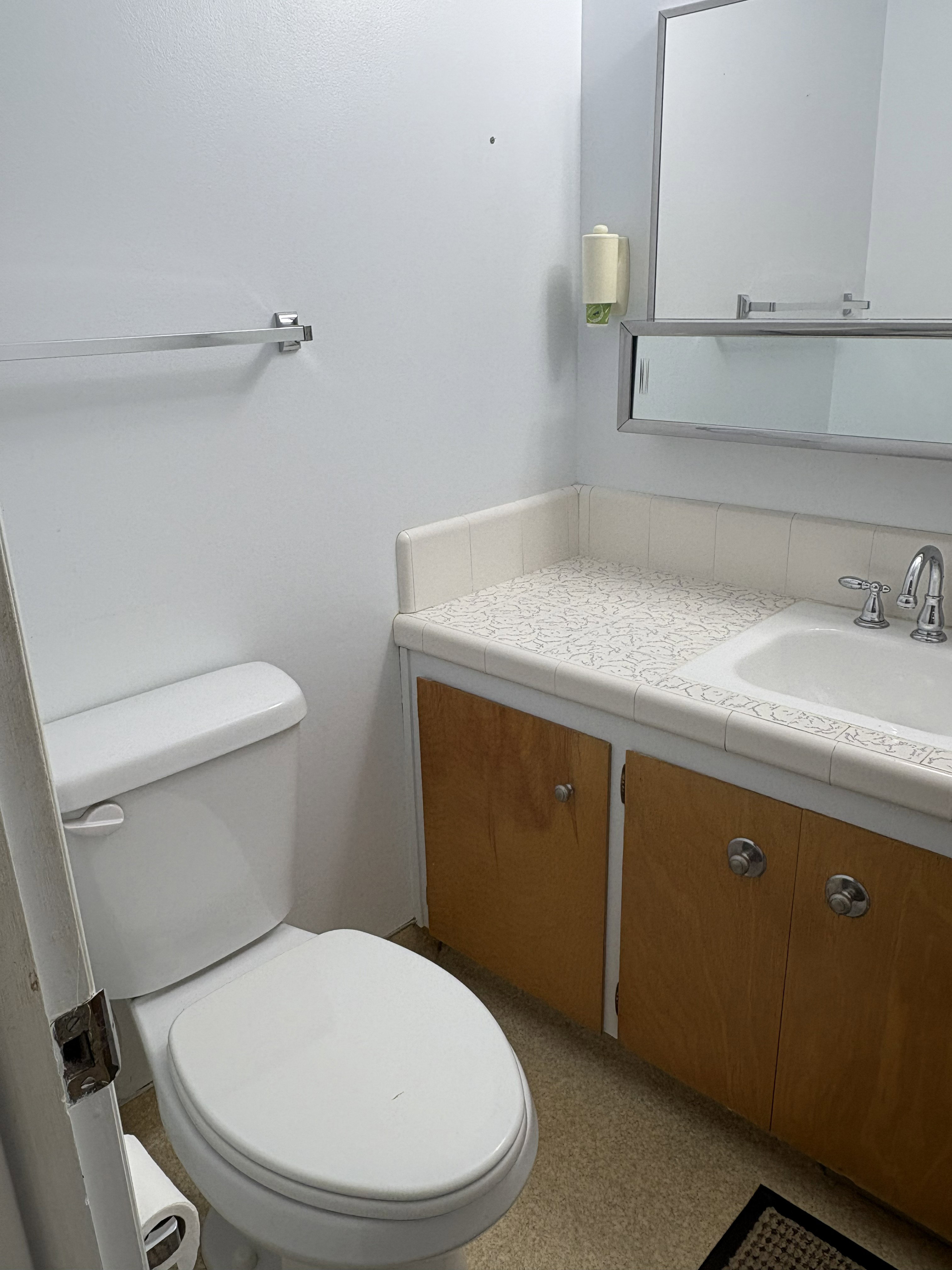 Bathroom with a white toilet and a vanity featuring light wood-finish cabinetry, a patterned countertop, and a white sink with a chrome faucet