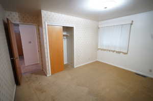 Unfurnished bedroom featuring light colored carpet, a closet, and wallpapered walls