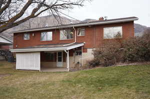 Back of house with a patio area, a chimney, a lawn, and brick siding