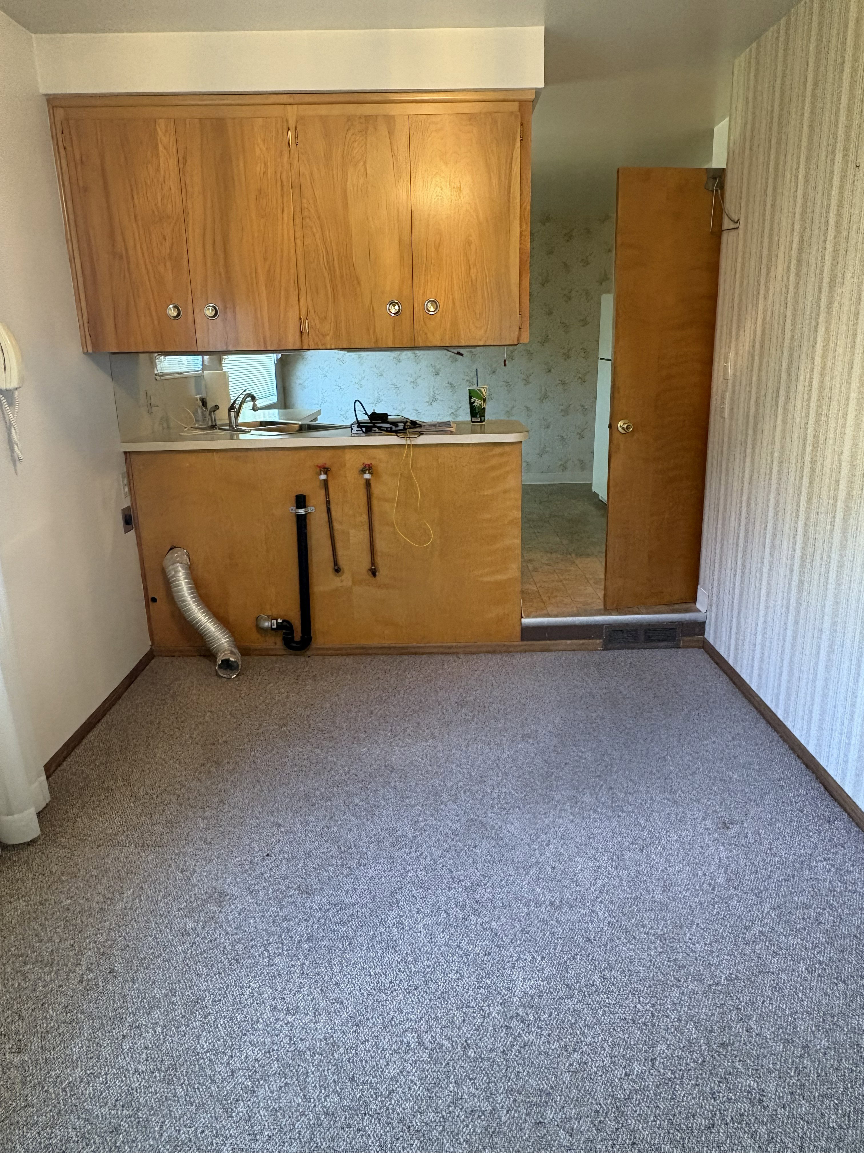 Laundry area with light-toned wood-finish cabinetry, a utility sink, and wall-mounted plumbing
