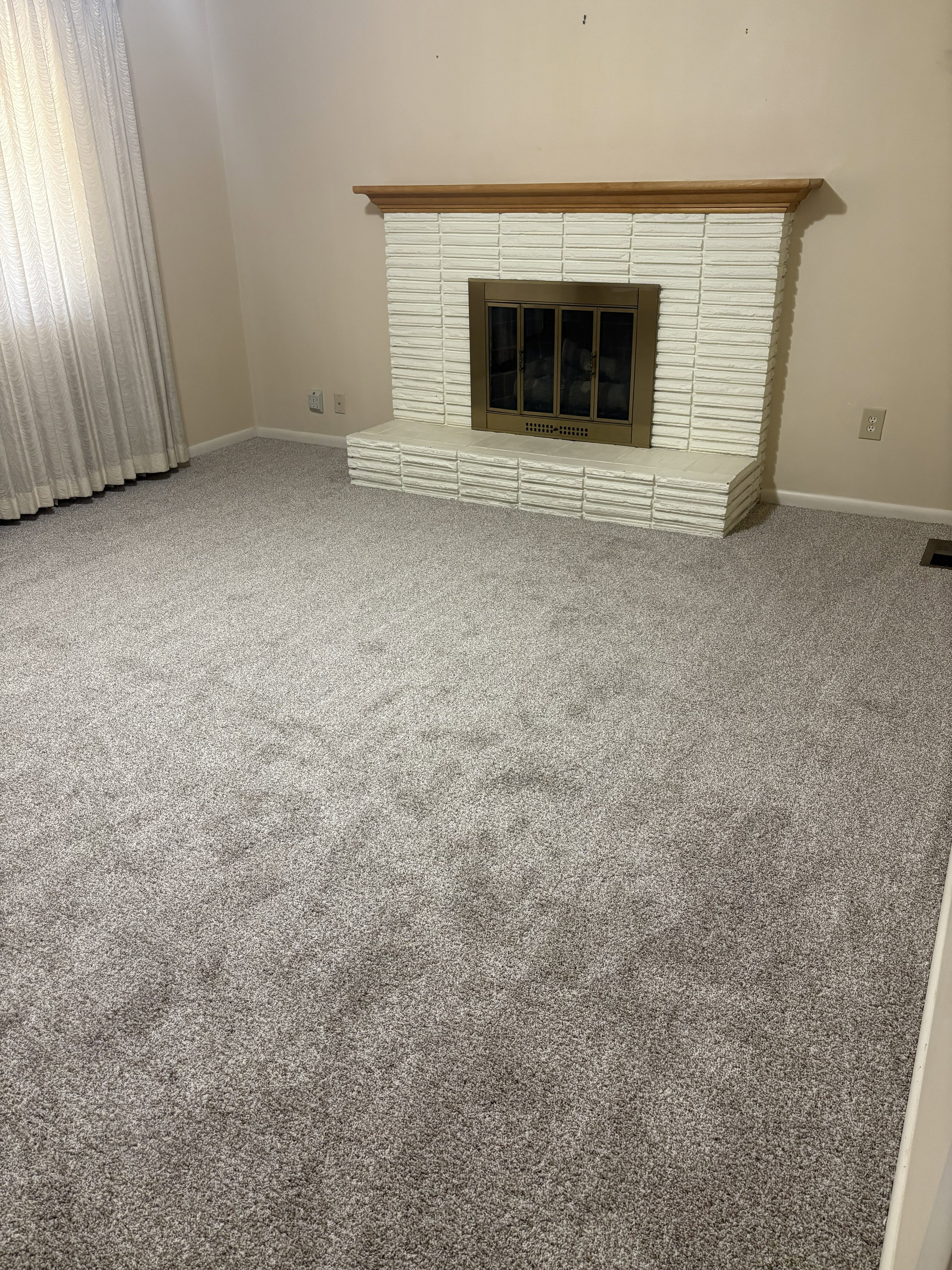 Living area featuring a white painted brick fireplace with a wood mantel, a brass-toned fireplace insert, and light gray wall-to-wall carpet