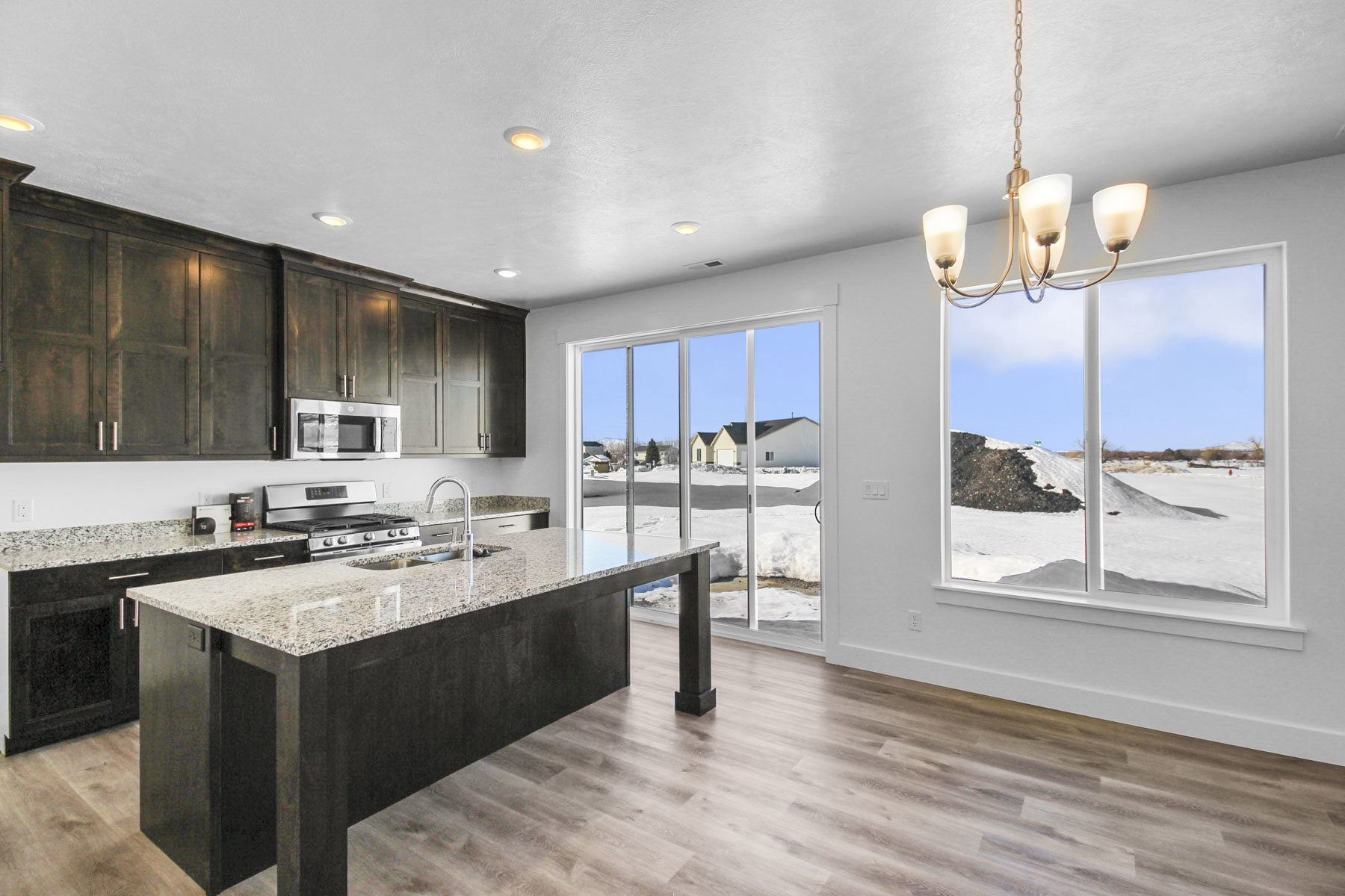 Kitchen with light stone counters, stainless steel appliances, hanging lights, an island with sink, and light wood-type flooring